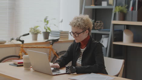 young woman with prosthetic arm using laptop in office