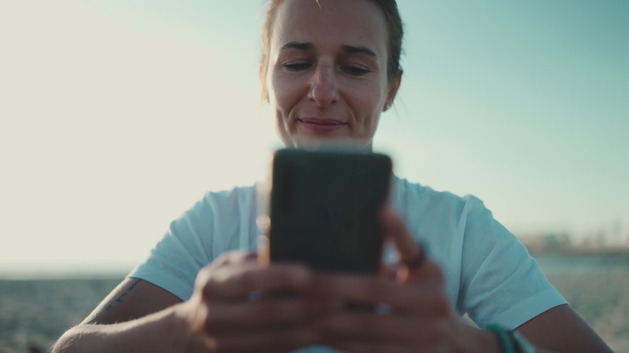 una deportista sentada usando su teléfono inteligente en la playa.
