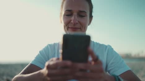 Sportlerin-Sitzt-Mit-Ihrem-Smartphone-Am-Strand.