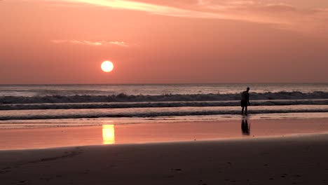 Sunset-at-Playa-Maderas-beach-in-Nicaragua-with-man-throwing-stones-at-the-surf,-Handheld-wide-shot