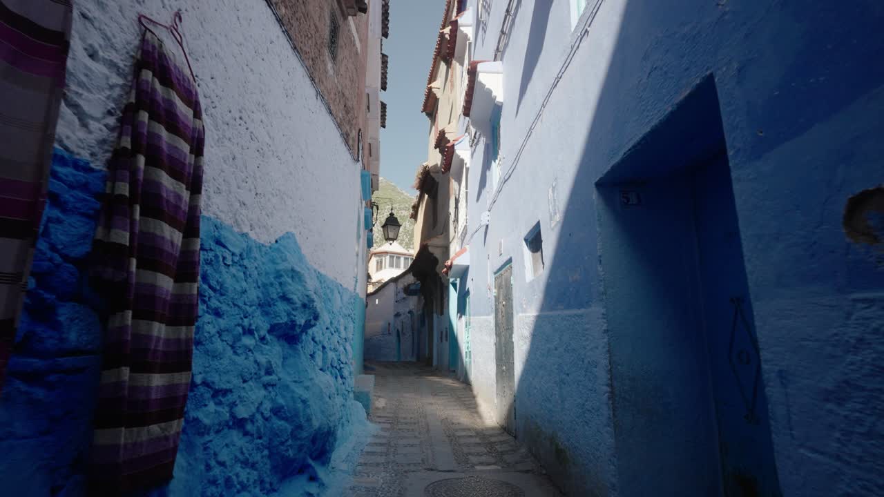 Vibrant fabrics hang on a wall along a narrow blue alleyway in Chefchaouen, Morocco’s blue city.
