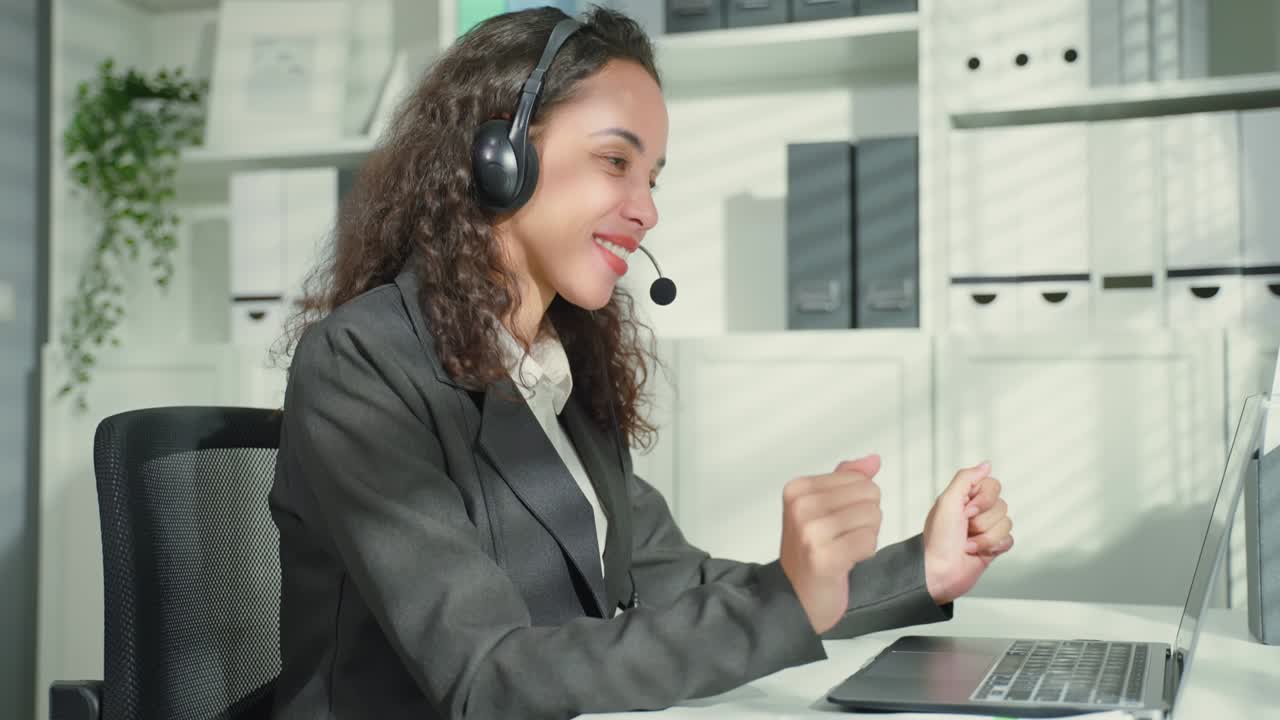 Donna d'affari latina che balla mentre lavora fino a tardi in ufficio di notte. Bella impiegata professionista in abbigliamento formale siede sulla scrivania al suo posto di lavoro, usa il computer portatile, ascolta musica e canta