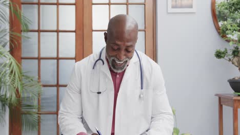 African-american-male-doctor-sitting-at-desk-and-having-video-call,-slow-motion