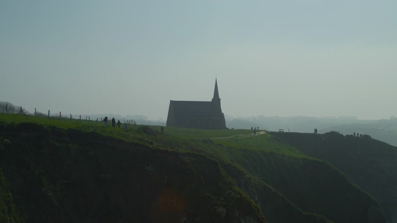 Klippekirke, gresskledd landskap, mennesker, statisk håndholdt opptak. Naturskjønn utsikt over historisk kapell på en stor grønn kysthøyde med turister som går utendørs