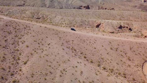 aerial view away from a car parked on a desert dirt road, in sunny kingman wash, usa - pull back, drone shot