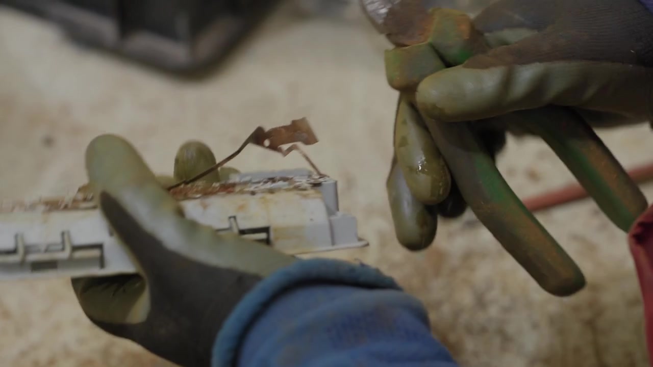 Gloved worker hands separating metal pieces from plastic components on factory floor