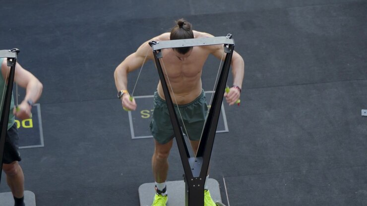 Male athlete powers through a SkiErg station during an intense HYROX fitness race showcasing cardiovascular endurance upper body strength speed and athletic conditioning