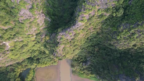 sampan tourist boat on ngo dong river entering cave limestone gorge of ninh binh national park, vietnam - aerial tracking top down view