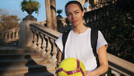 camera zooming on soccer woman with backpack playing with a ball in hands.