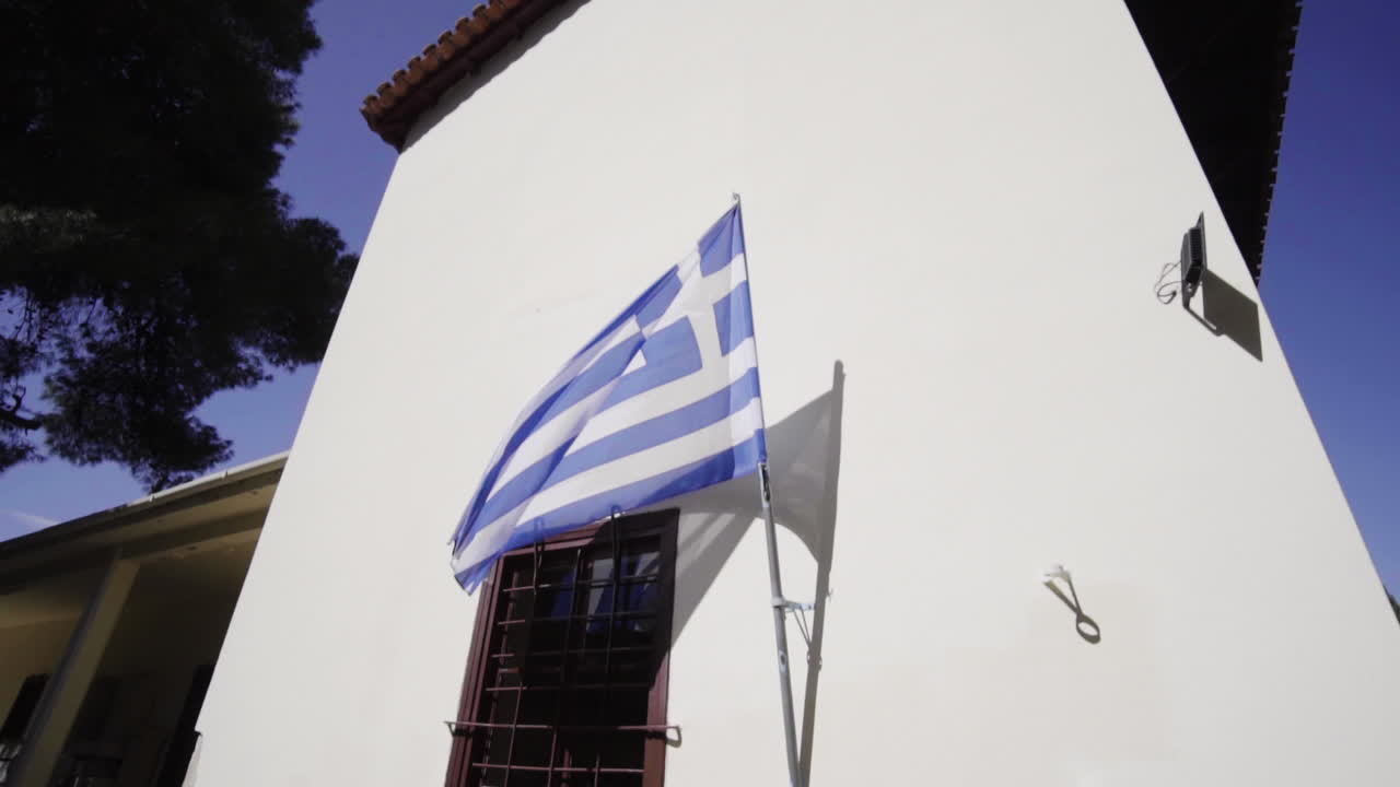 Griechische Flagge an einer weißen Wand, die im Wind weht – Aufnahme aus der Froschperspektive.