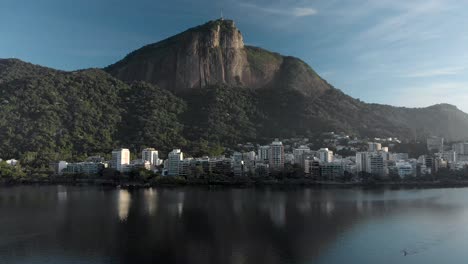 slow aerial approach of the corcovado mountain in rio de janeiro at sunrise seen from and mirrored in the city lake