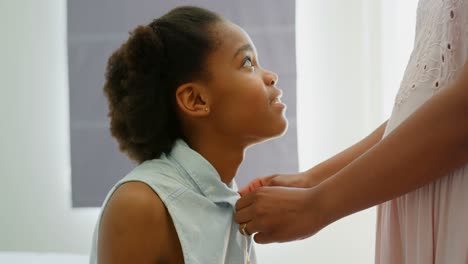 Side-view-of-mid-adult-black-mother-helping-her-daughter-in-wearing-dress-in-a-comfortable-home-4k