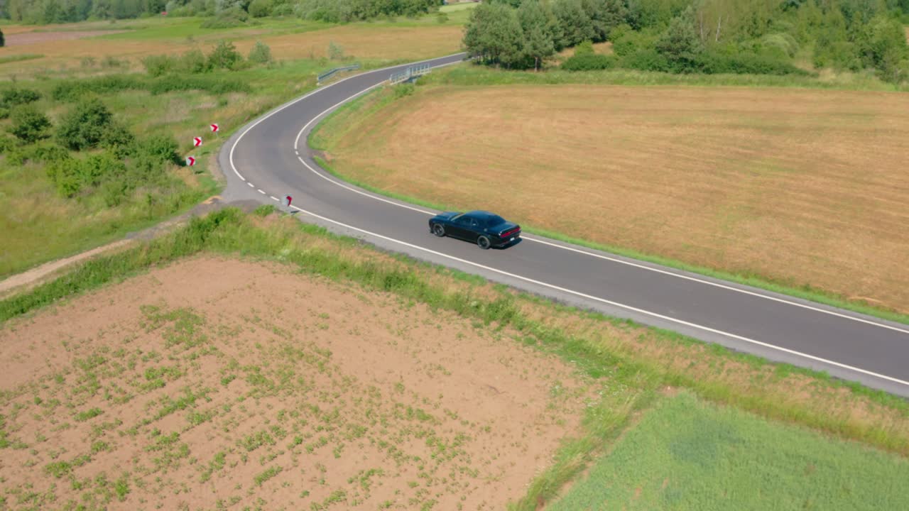Iconic American muscle car, a dark Dodge Challenger Scat Pack, cruising through scenic rural landscapes. Perfect for content about classic cars, road trips, and the American spirit.