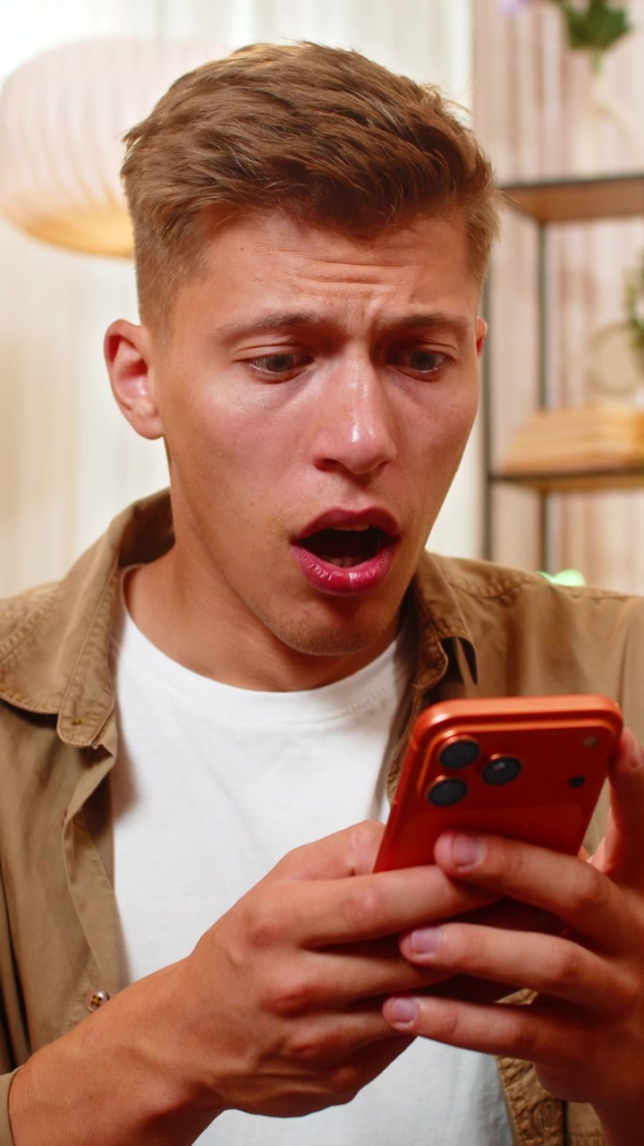 Young man on home sofa reading bad message on smartphone feeling sad shocked and desperate indoors