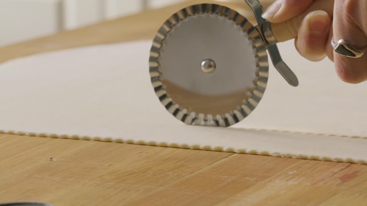 Hand Cutting Dough with Fluted Pastry Wheel Cutter on Kitchen Table