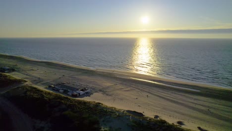 Pull-back-aerial-view-of-sunset-over-Kijkduin-Beach,-Netherlands