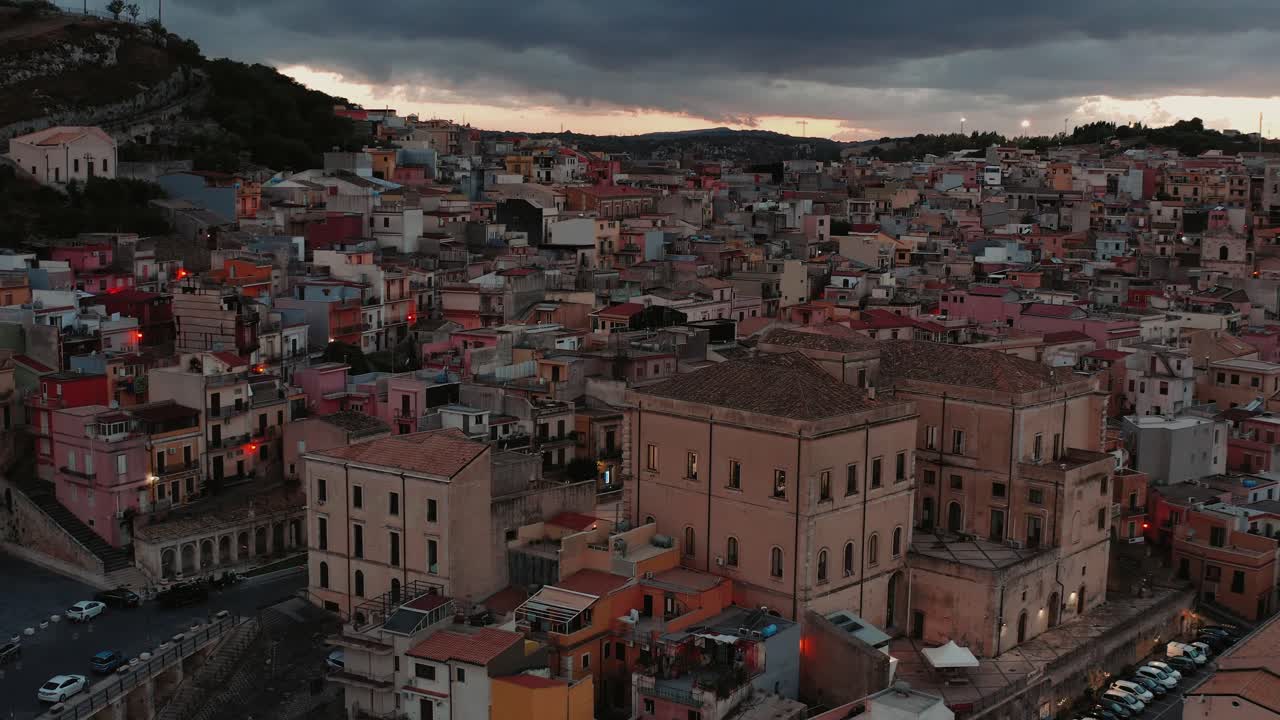 La ciudad en la cima de la colina de Melilli, Sicilia, brilla cálidamente mientras las luces de la ciudad se encienden al anochecer.