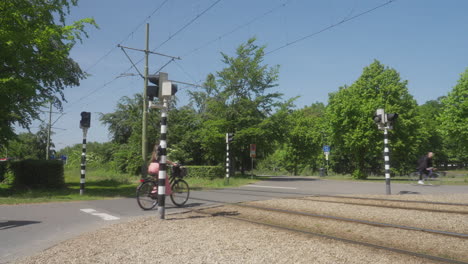 a tram passes a crossing close to the central of station of the hague, netherlands. after the tram passes, cyclists pass by.