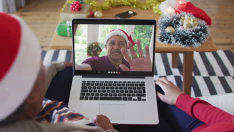 madre y hija afroamericanas usando una computadora portátil para una videollamada de navidad con un hombre en la pantalla