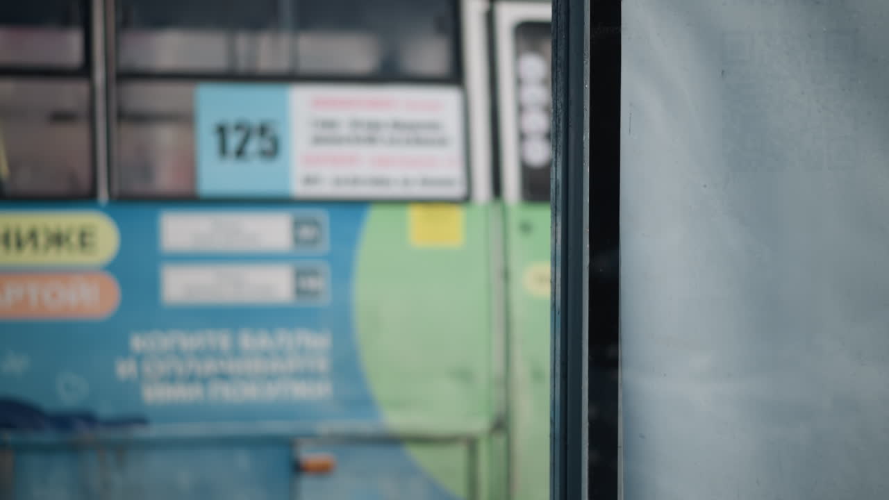 winter commuter in hooded coat passes bus stop shelter window, city buses glide along snowy street beyond, blurred buildings and road lines create motion feel, quiet urban transit