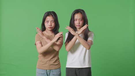 young asian women victims of violence with bruise on bodies looks into camera showing hands cross gesture to stop violence in green screen background studio