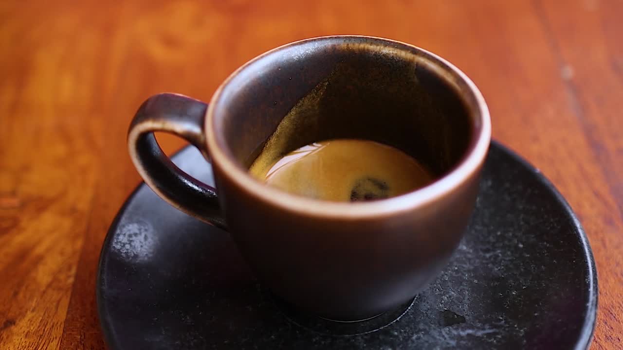 Una mano posiziona con cura una tazza da caffè espresso in ceramica scura su un piattino nero abbinato