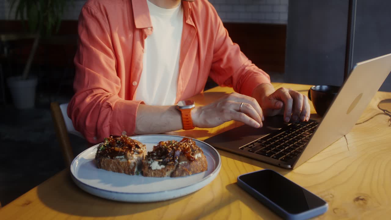 hombre trabajando en una cafetería, disfrutando del almuerzo y usando una computadora portátil