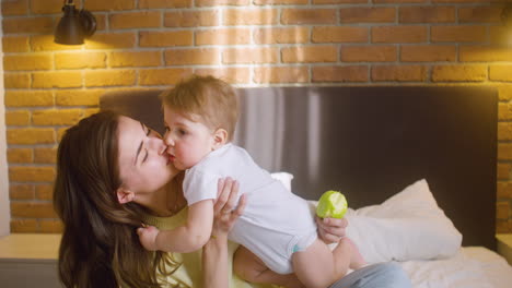 Woman-Holding-Her-Baby-And-Kissing-Him-While-Sitting-On-The-Bed-At-Home