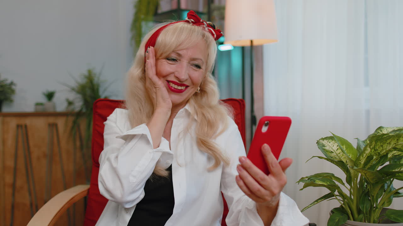 abuela mayor en la silla de casa usar el teléfono inteligente celebrar gran gran lotería ganar el premio mayor, buenas noticias