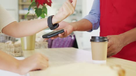 video of hands of biracial woman paying with smartwatch for baguette