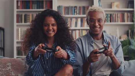 happy mixed race couple sitting on sofa playing video games using controllers