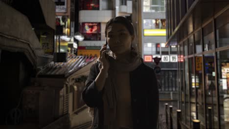 frustrated woman walking along dark city street at night making call on mobile phone