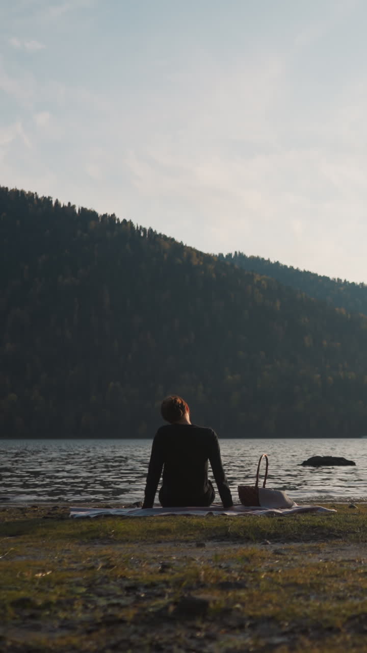 una mujer gira la cabeza para aliviar el dolor descansando en la orilla del río después de la puesta del sol. una mujer con una canasta de comida disfruta de un picnic sola en la belleza intacta de la naturaleza al crepúsculo en la noche de otoño