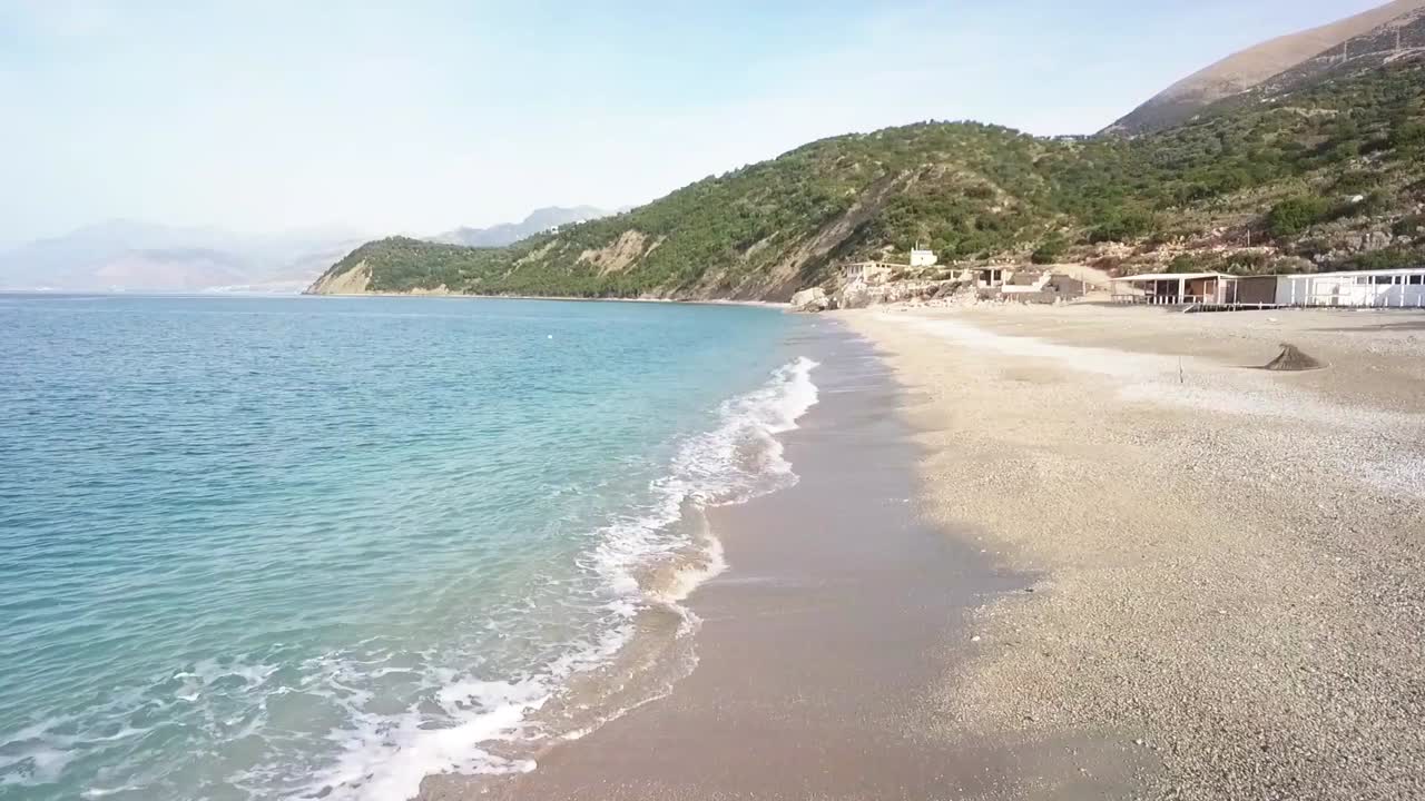 Waves crashing in on Lukova Beach along the Albanian Rivera during a summer day with mountains in the background