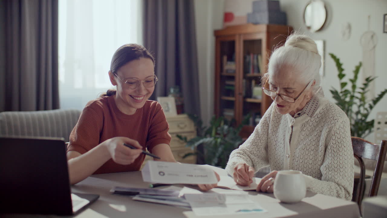 Female Caregiver Assisting Elderly Woman with Financial Documents at Home