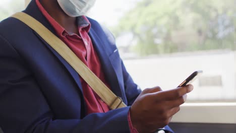 Hands-of-african-american-man-in-city-wearing-face,-using-smartphone-in-bus