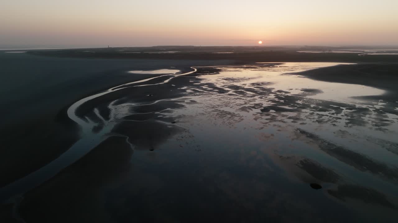Pullback aerial reveals wide mudflats and channels as a boat sits near the edge during first light. Wadden Sea