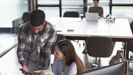 young caucasian woman and asian man collaborate over a tablet in a business office setting