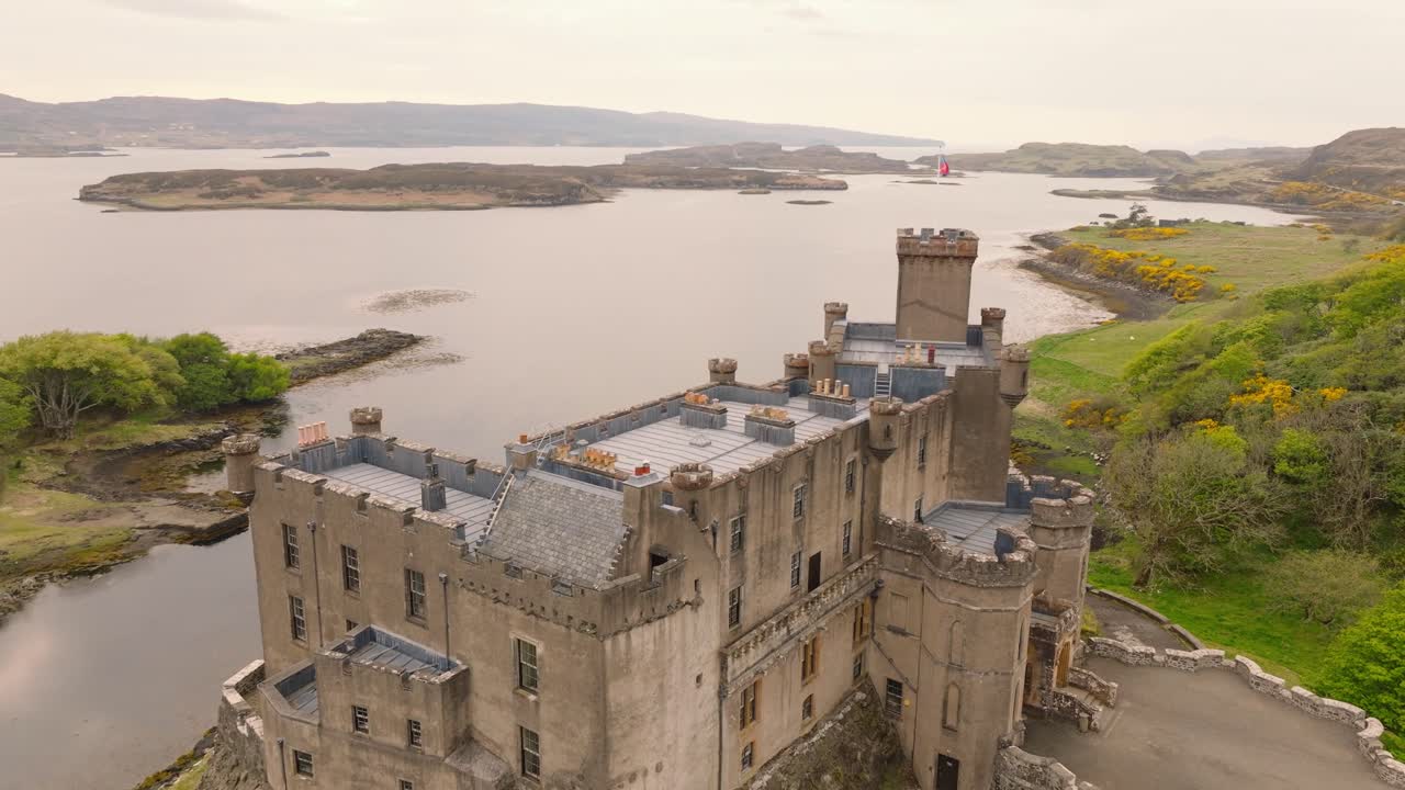 Aerial drone shot of Dunvegan Castle on the Isle of Skye, Scotland, with a scenic bay in the background, surrounded by lush greenery and rugged coastal beauty