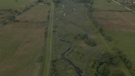 Drohne-Fliegt-Einem-Kleinen-Lokalen-Fluss-Nach-Und-Enthüllt-Wunderschöne-Grüne-Feldlandschaften-Im-Dorf-Debki-In-Nordpolen