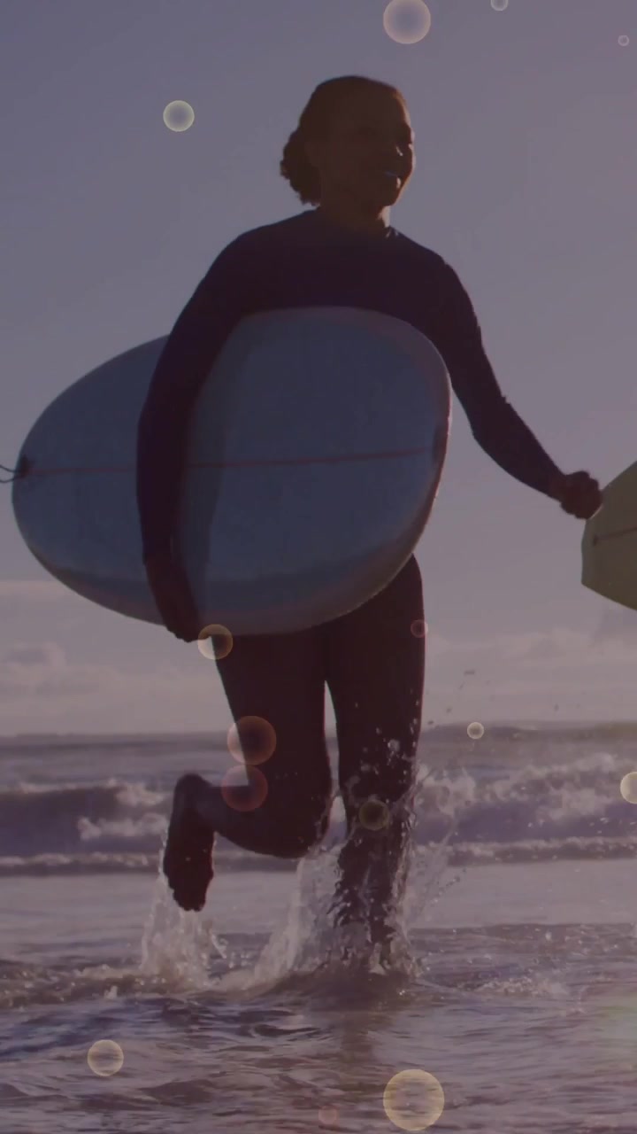 Video verticale: Surfista donna che esce dal mare dopo una sessione, con un effetto di bolle sportive sovrapposto sulle tavole.
