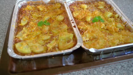 two trays of freshly baked potatoes with pork topped with cheese - zoom-out shot