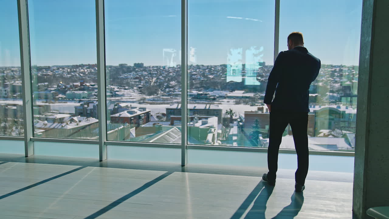 Young businessman talking the phone in office. Handsome entrepreneur in suit walking near large office windows and having a phone conversation.