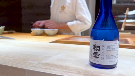 chef prepares sushi with sake bottle nearby