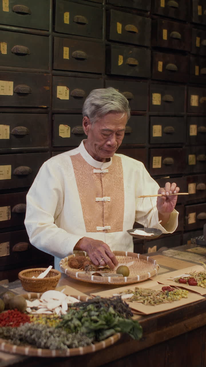 Vertical of Elderly Healer Weighing Dried Herbs on Scales at Pharmacy