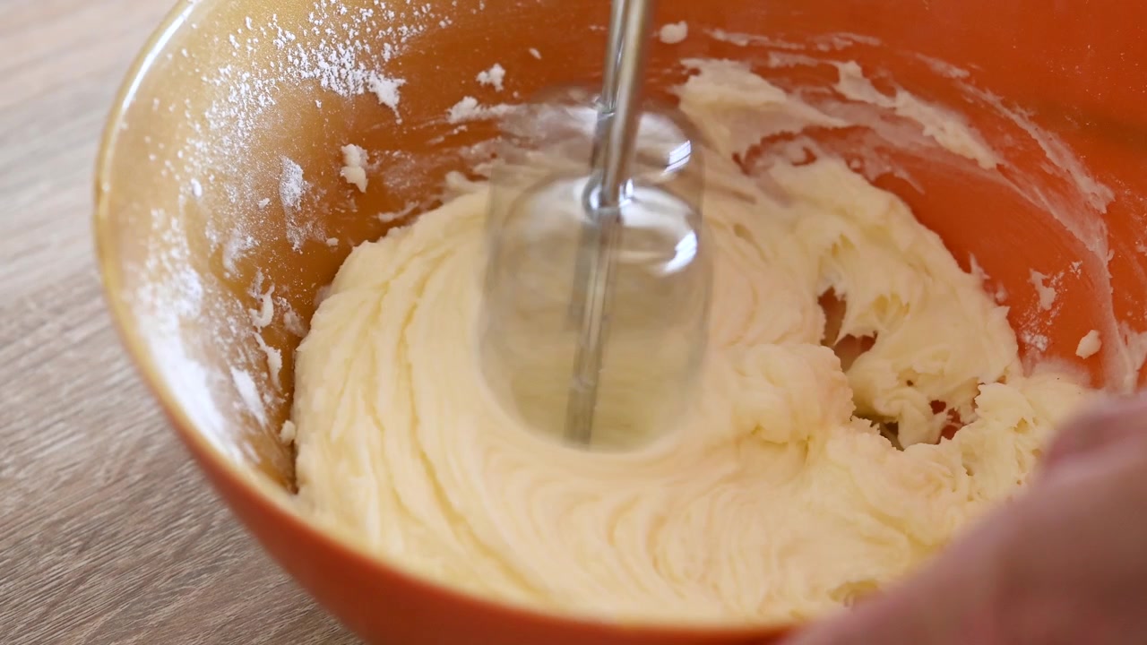 Electric Mixer Blending Creamy Batter in an Orange Bowl