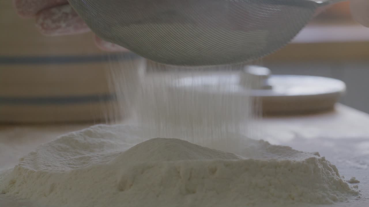Hands of Cook Sifting Flour on Table in the Kitchen