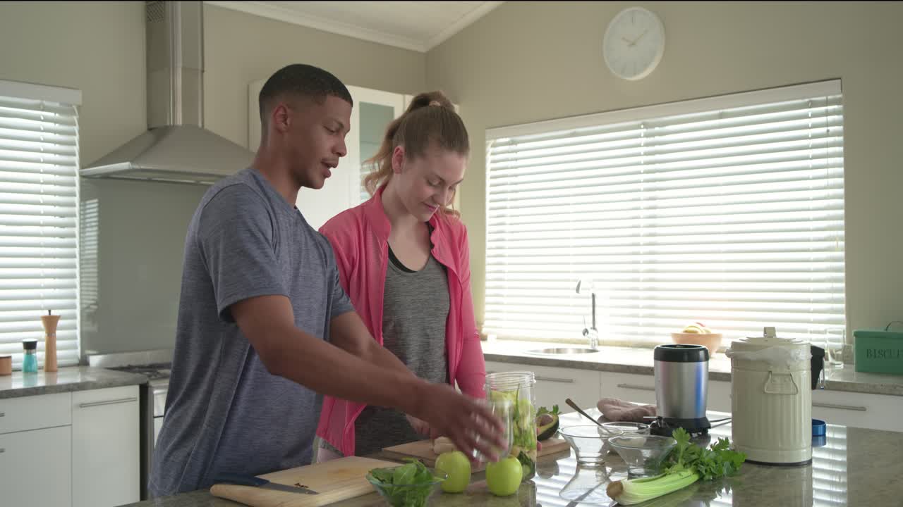 Casal cortando e adicionando folhas verdes no copo do liquidificador na ilha da cozinha para fazer um smoothie verde