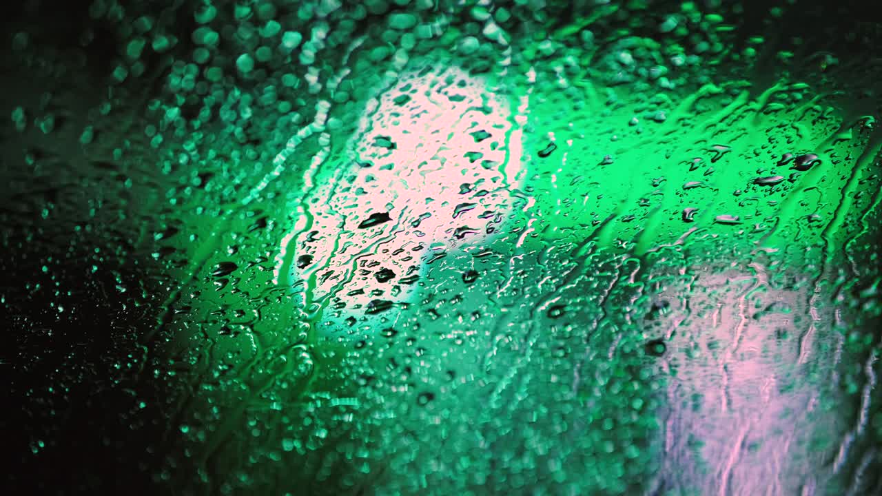 cerca de las gotas de agua de lluvia en el vidrio de la ventana del coche con luces de tráfico borrosas de fondo por la noche.
