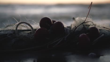 slow motion reverse shot of water sea revealing a fisherman's net left abandoned on the shoreline during the golden hour - blurry background